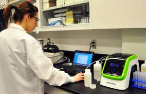 Female standing in a laboratory using the PeCOD Analyzer to run samples for chemical oxygen demand analysis.