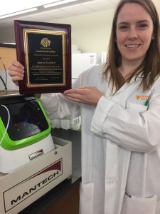 Amina Stoddart standing with the peCOD analyzer and her ASTM International Standards Development Award